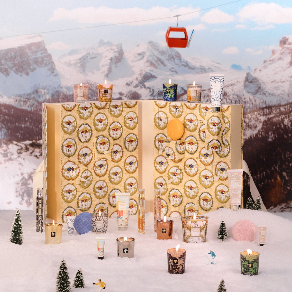 Baobab Advent Calendar Voyage Extraordinaire: opened gold book-shaped calendar with mini candles and body care in a snowy mountain scene, 24 doors